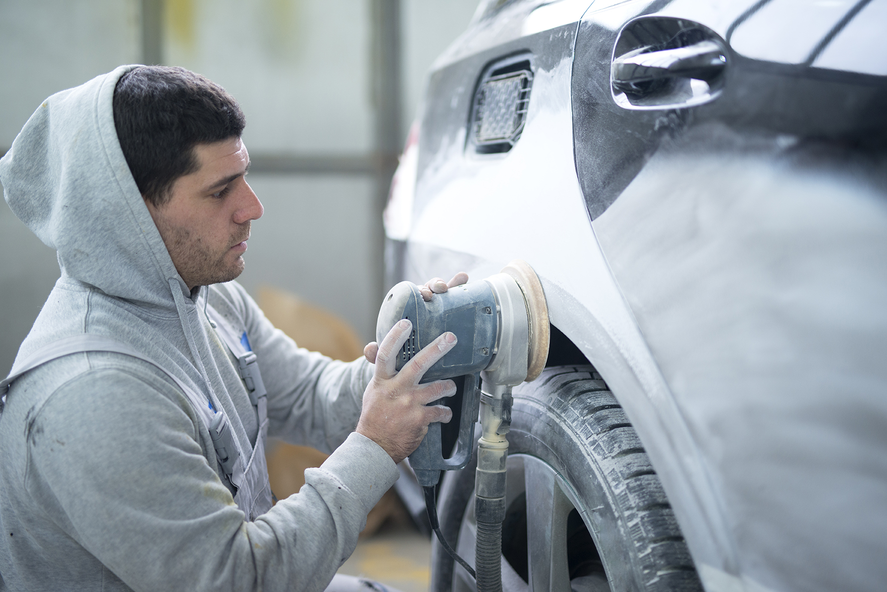 Auto repairman grinding car body with a machine preparing vehicl