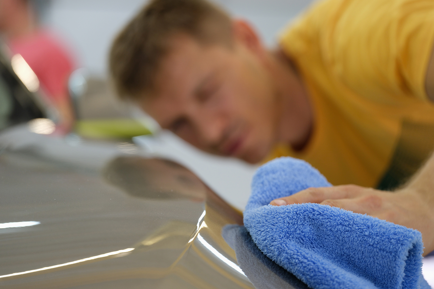 Repairman wiping hood of car with microfiber cloth closeup